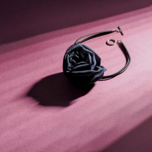 Black silk chiffon rose choker necklace with toggle clasp, photographed on a purple background with soft shadows.