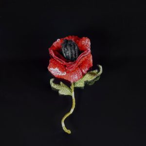 Close-up of a handmade 3D red poppy brooch with sequin petals, velvet-lined back, and embroidered leaves, shown on a black background