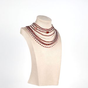 Angled view of handmade red and white multi-strand necklace featuring glass beads, mother of pearl beads, and larger focal beads with gold outlines, displayed on a mannequin bust.