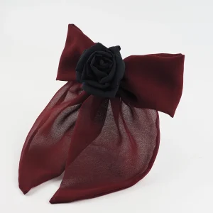 A handcrafted burgundy chiffon bow hair accessory with a black silk rose at the center, featuring a structured yet delicate design. The bow is attached to a metal hair clip, making it a bold and elegant choice for styling