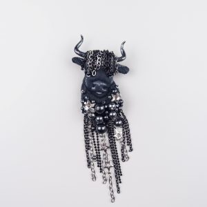 Close-up of handmade Taurus textile brooch featuring black embroidery, custom horns, glossy beads, and chain fringe with rhinestones